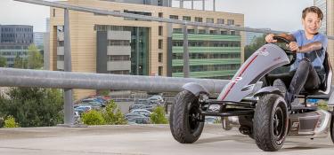 Boy riding a BERG XL Race pedal go-kart on an elevated parking lot in the city, banner