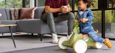 Banner with child on a green BERG GO2 ride-on car in a modern living room