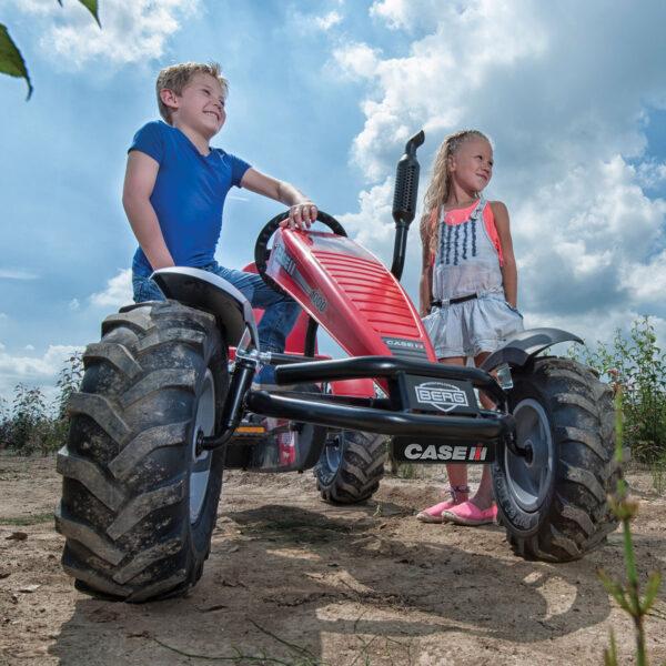 Dos niños juegan al aire libre con el BERG XL Farm coche de pedales rojo con neumáticos de tractor resistentes