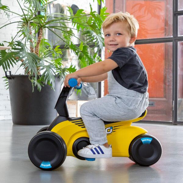 Blonde toddler rides the yellow BERG GO² ride-on car indoors