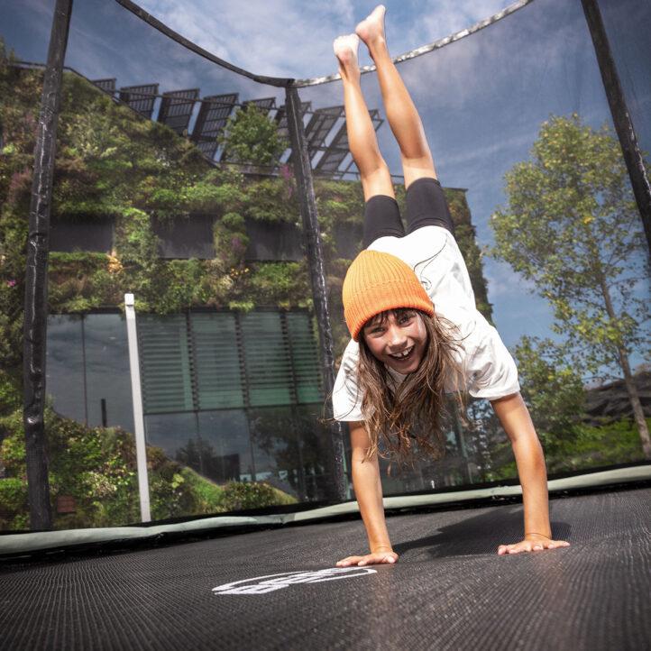 Girl performs a handstand on a BERG Champion ECO trampoline in a green environment