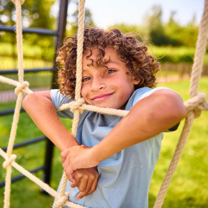 Child climbs on the BERG PlayBase climbing net and smiles at the camera