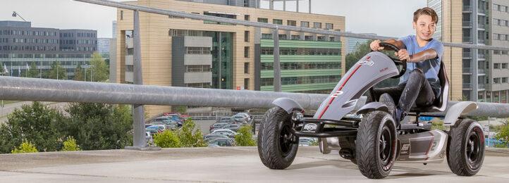 Boy riding a BERG XL Race pedal go-kart on an elevated parking lot in the city, banner