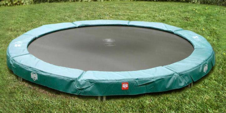 Geïnstalleerde BERG inground trampoline met groene beschermrand in een tuin