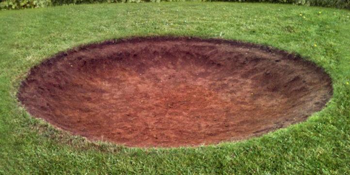 Volledig uitgegraven kuil in het gras als voorbereiding voor de installatie van een BERG inground trampoline