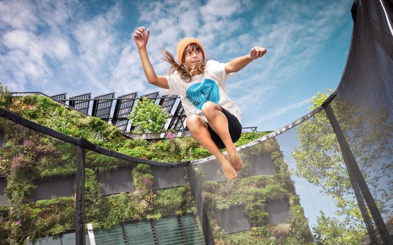 Enfant saute sur un trampoline BERG Champion avec une façade verte en arrière-plan