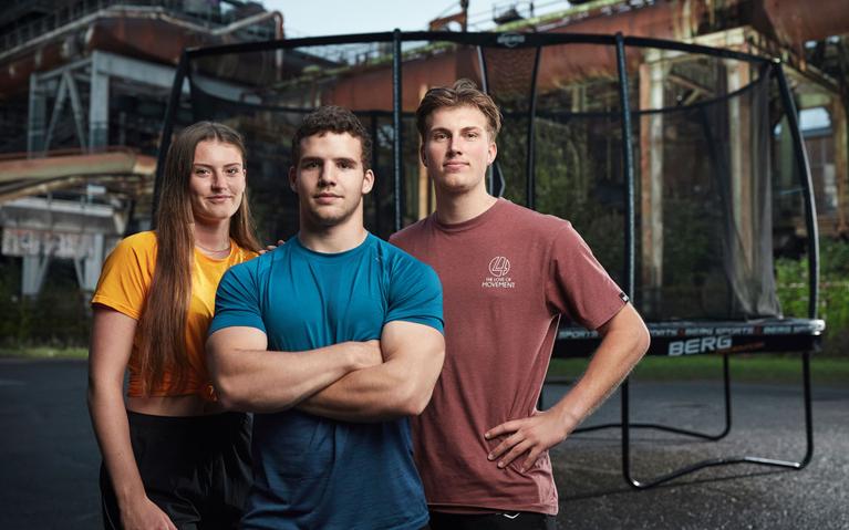 Trois athlètes posent devant un trampoline BERG dans un décor industriel