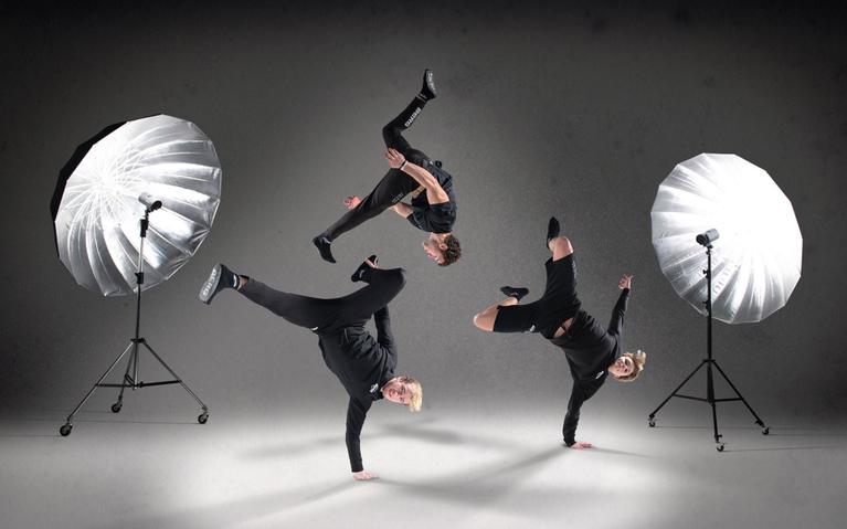 Three breakdancers performing spectacular moves in a studio with large softbox lights