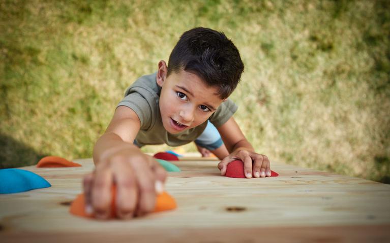 Junge klettert auf einem BERG PlayBase Klettergerüst mit Holzkletterwand