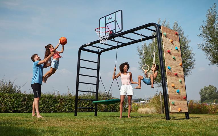 Børn leger på et BERG PlayBase klatrestativ med basketballkurv, gynge og klatrevæg i haven