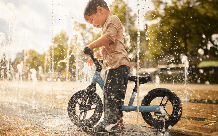 Child plays with a BERG MOOV 7 balance bike near fountains