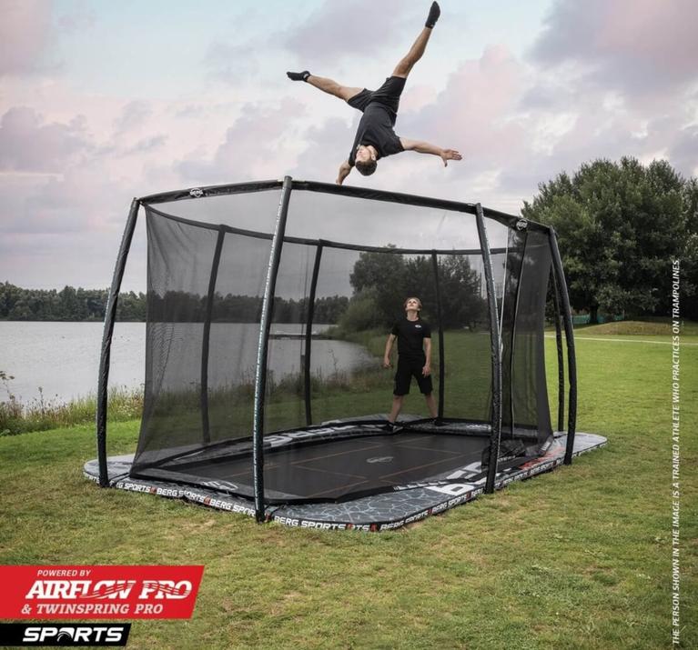 Professioneller Springer macht einen Salto auf einem rechteckigen BERG Pro Bouncer Trampolin Sports mit AirFlow Pro und TwinSpring Pro an einem See