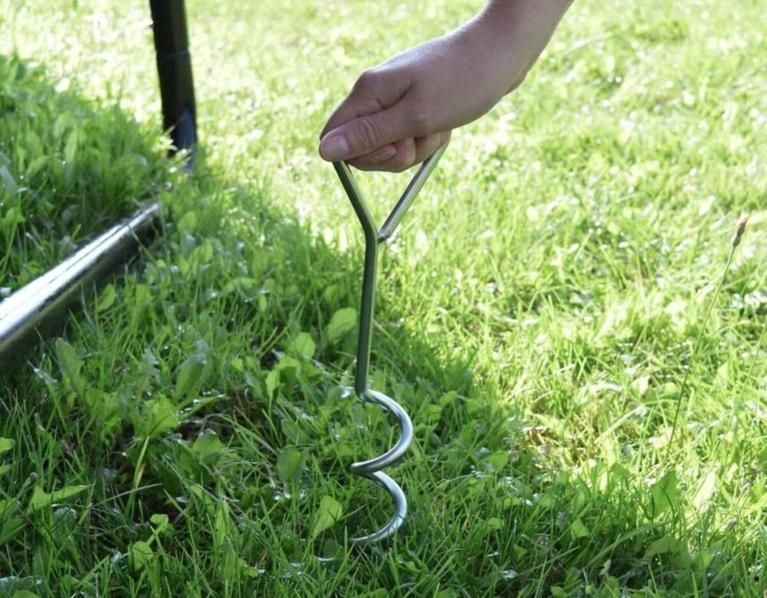 Hand befestigt ein BERG Trampolinanker im Gras für zusätzliche Stabilität