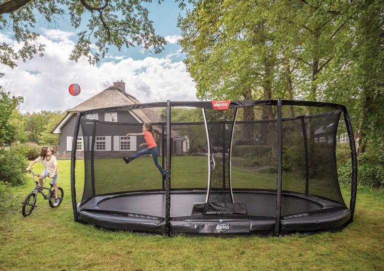 Kind springt auf einem ovalen BERG inground Trampolin mit Netz in einem grünen Garten