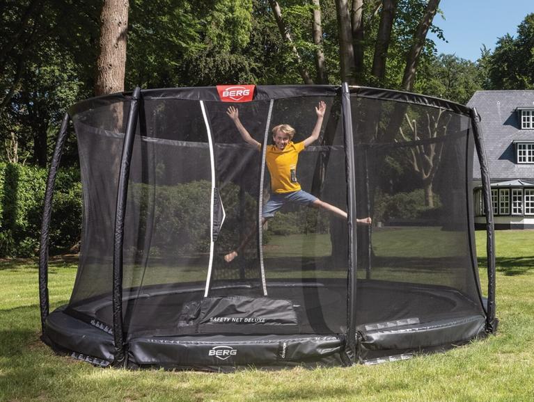 Kind springt auf einem runden BERG Trampolin mit Netz in einem grünen Garten