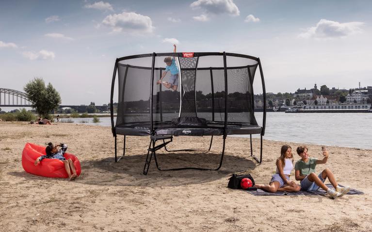 Niño salta en un trampolín BERG - B2B en la playa, mientras los amigos se relajan