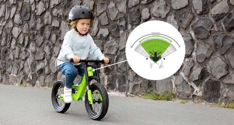 Child on a BERG Biky balance bike with a safe steering system, riding along a stone wall