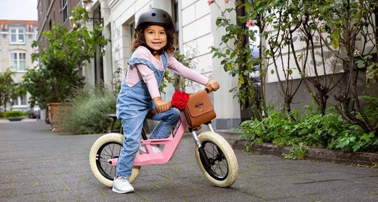 Child riding a pink BERG Biky Retro balance bike in an urban setting