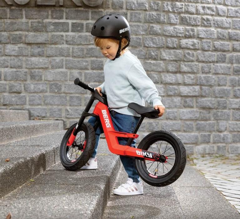 Child effortlessly lifts a red BERG Biky balance bike up the stairs