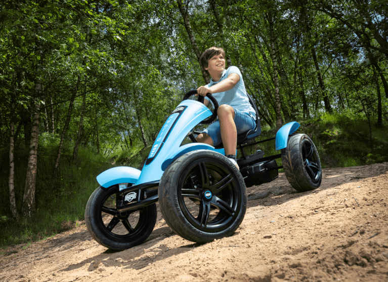 Niño conduciendo un kart a pedales eléctrico BERG XL por un sendero arenoso en el bosque