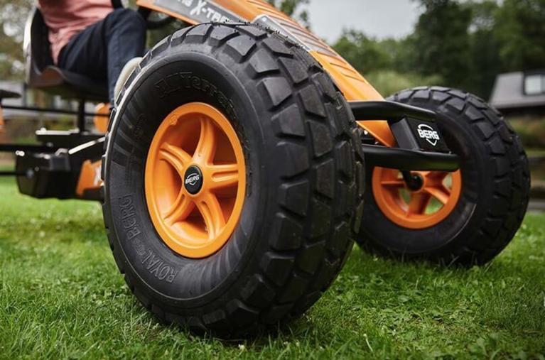 Primer plano de una rueda de kart a pedales BERG con neumáticos offroad y llantas naranjas sobre césped