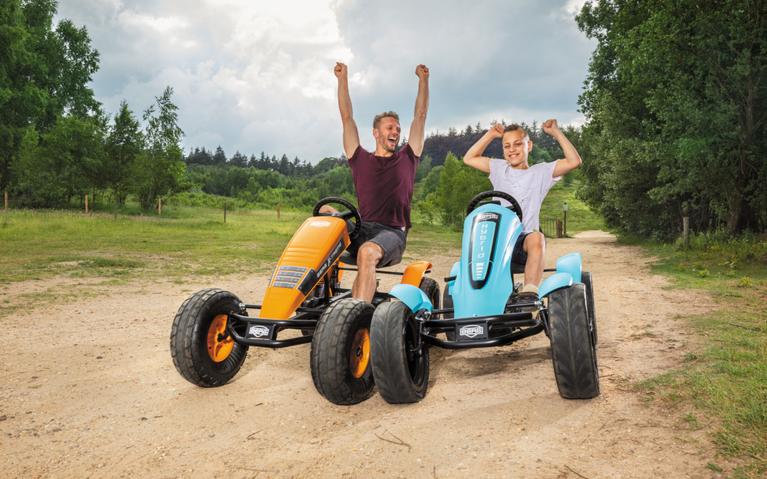 Adult and child cheering on BERG XL large pedal go-karts during a ride on a sandy path