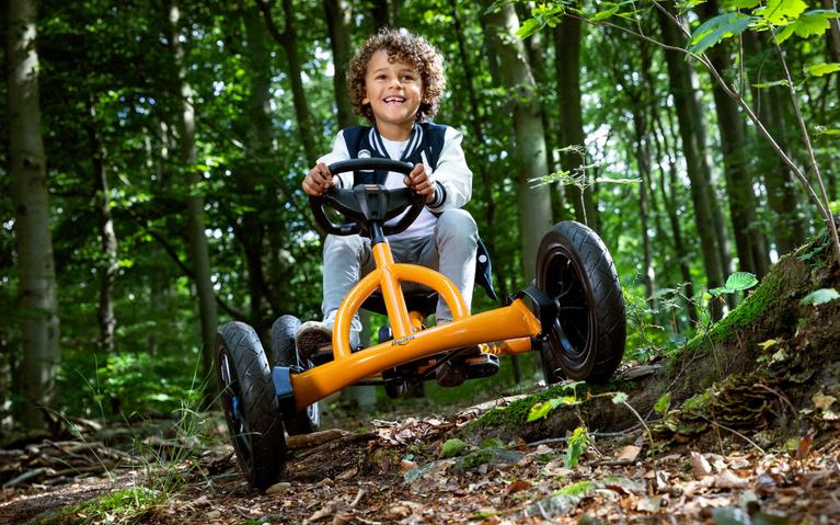 Happy child riding a BERG Buddy B-Orange pedal go-kart on a forest trail