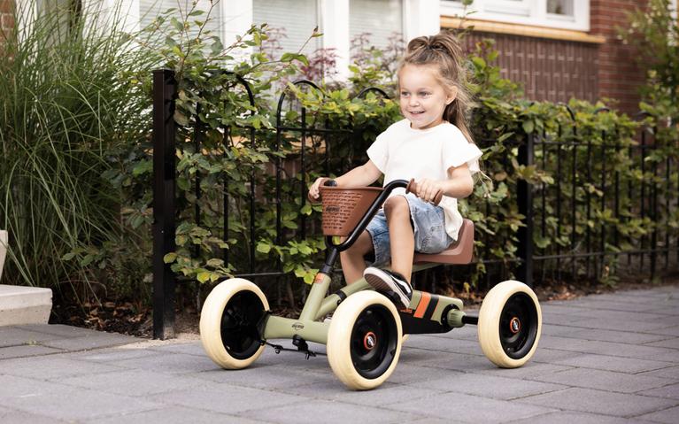 Happy girl riding a BERG Buzzy Retro pedal go-kart with a basket on a paved path