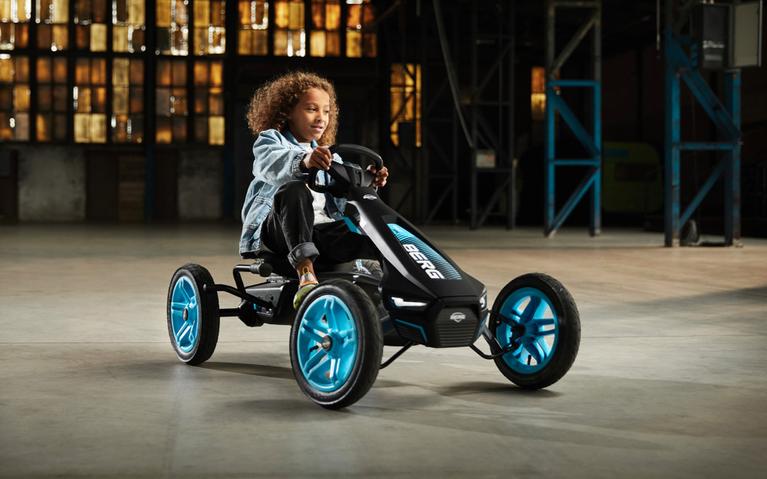 Happy child riding a BERG Rally APX Blue pedal go-kart in an industrial hall