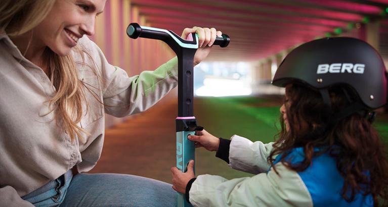 Parent helping child adjust the handlebar of a BERG Nexo scooter