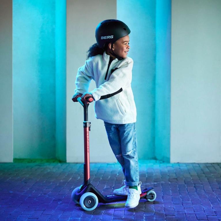 Child standing on a BERG Nexo scooter with illuminated wheels in an atmospheric setting