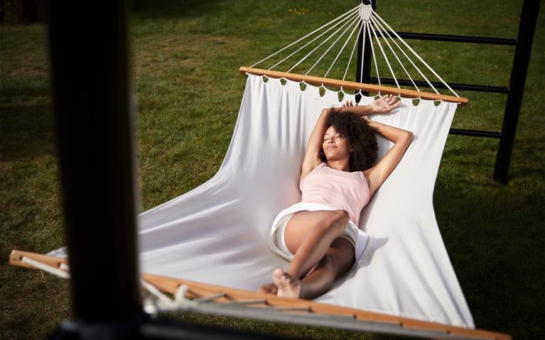 Woman relaxing in a hammock attached to a BERG PlayBase climbing frame in the garden