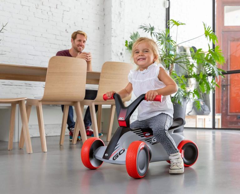 Child smiling while riding a grey-red BERG GO ride-on car indoors