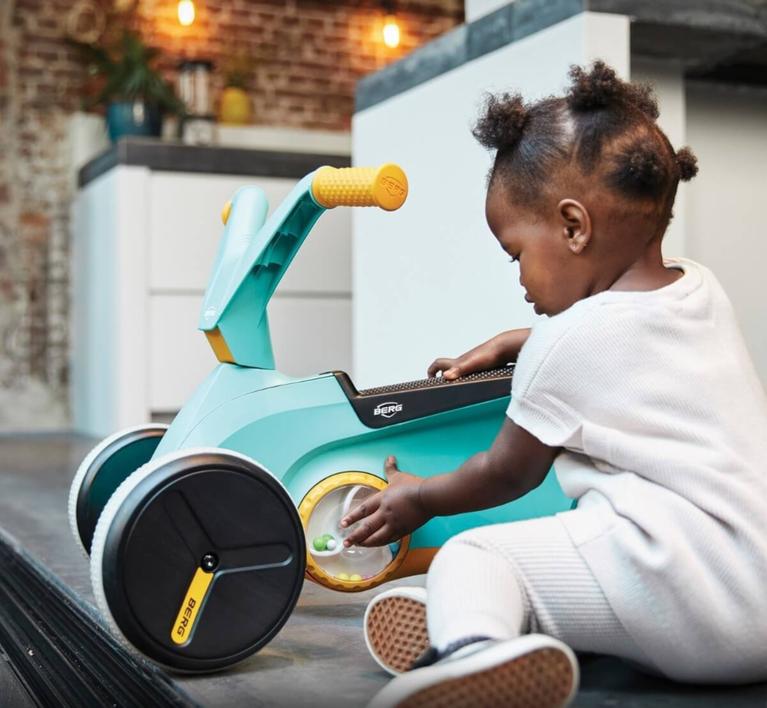 Child exploring a turquoise BERG GO Twirl ride-on car indoors