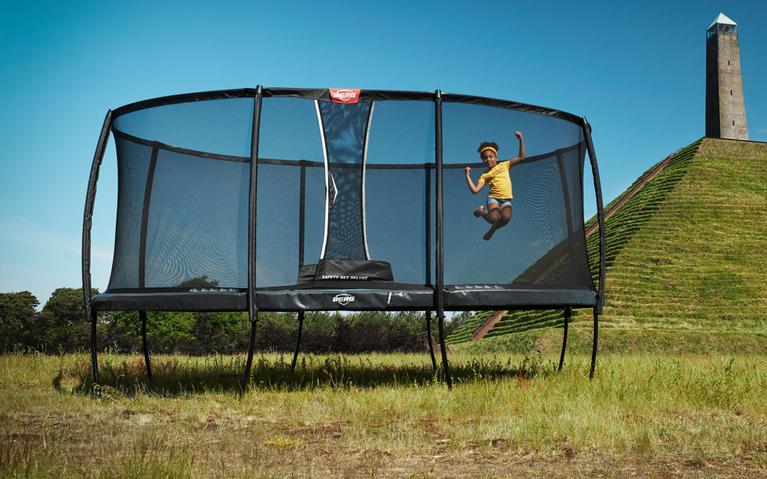 Child jumping on a BERG rectangular trampoline with net in a historic setting with a monument