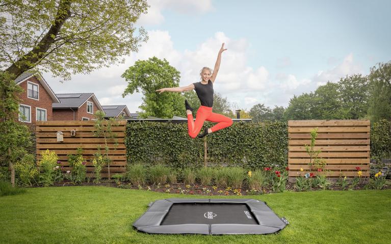 Woman jumping on a BERG Ultim FlatGround rectangular trampoline Sports in a garden