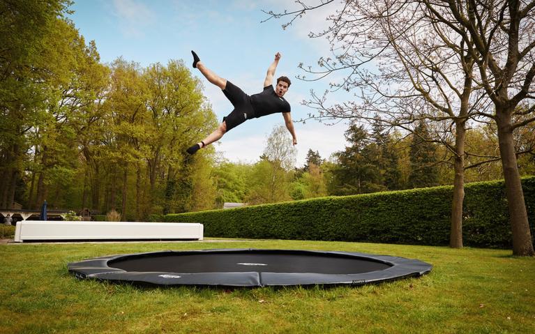 Saltador profesional realiza un salto en el aire en un trampolín BERG FlatGround Sports en un jardín