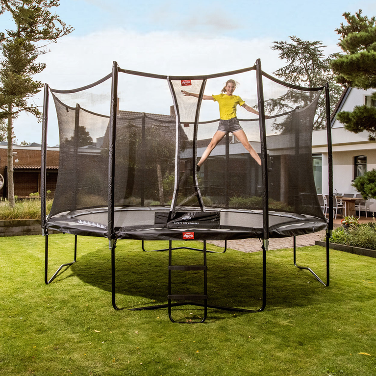 Child jumping on a BERG Favorit trampoline with safety net in a garden