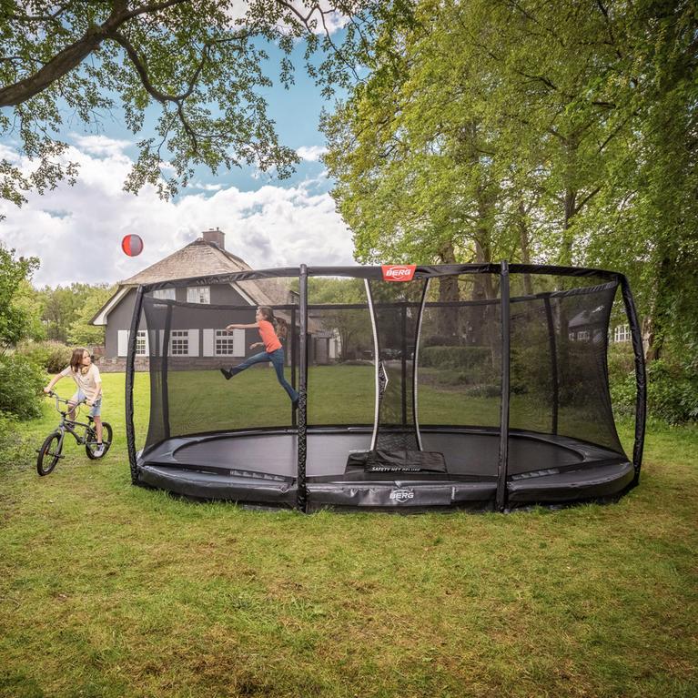 Child jumping on a BERG inground trampoline with safety net in a green garden