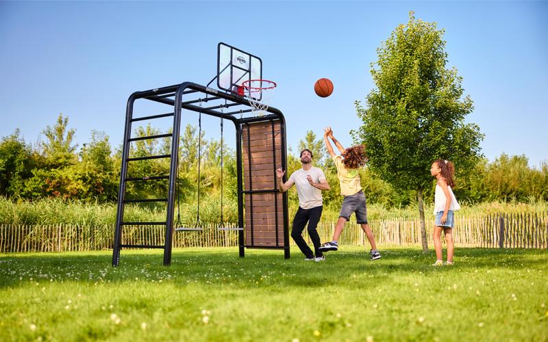 BERG PlayBase playset with basketball hoop and swings, where a father plays outside with his children.