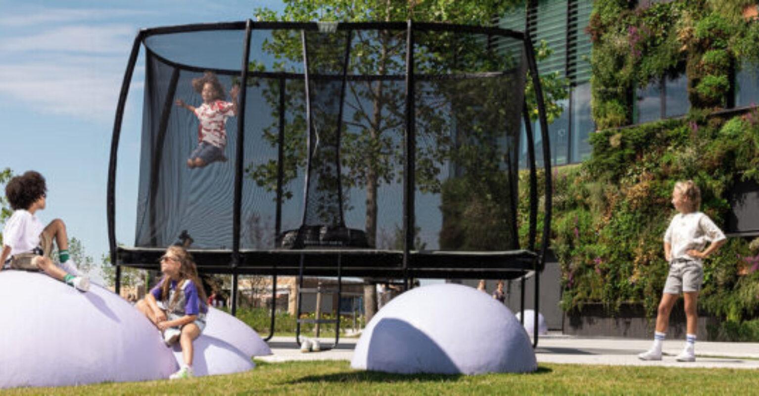 Bannière avec des enfants jouant autour d’un trampoline BERG Champion dans un espace de jeu moderne