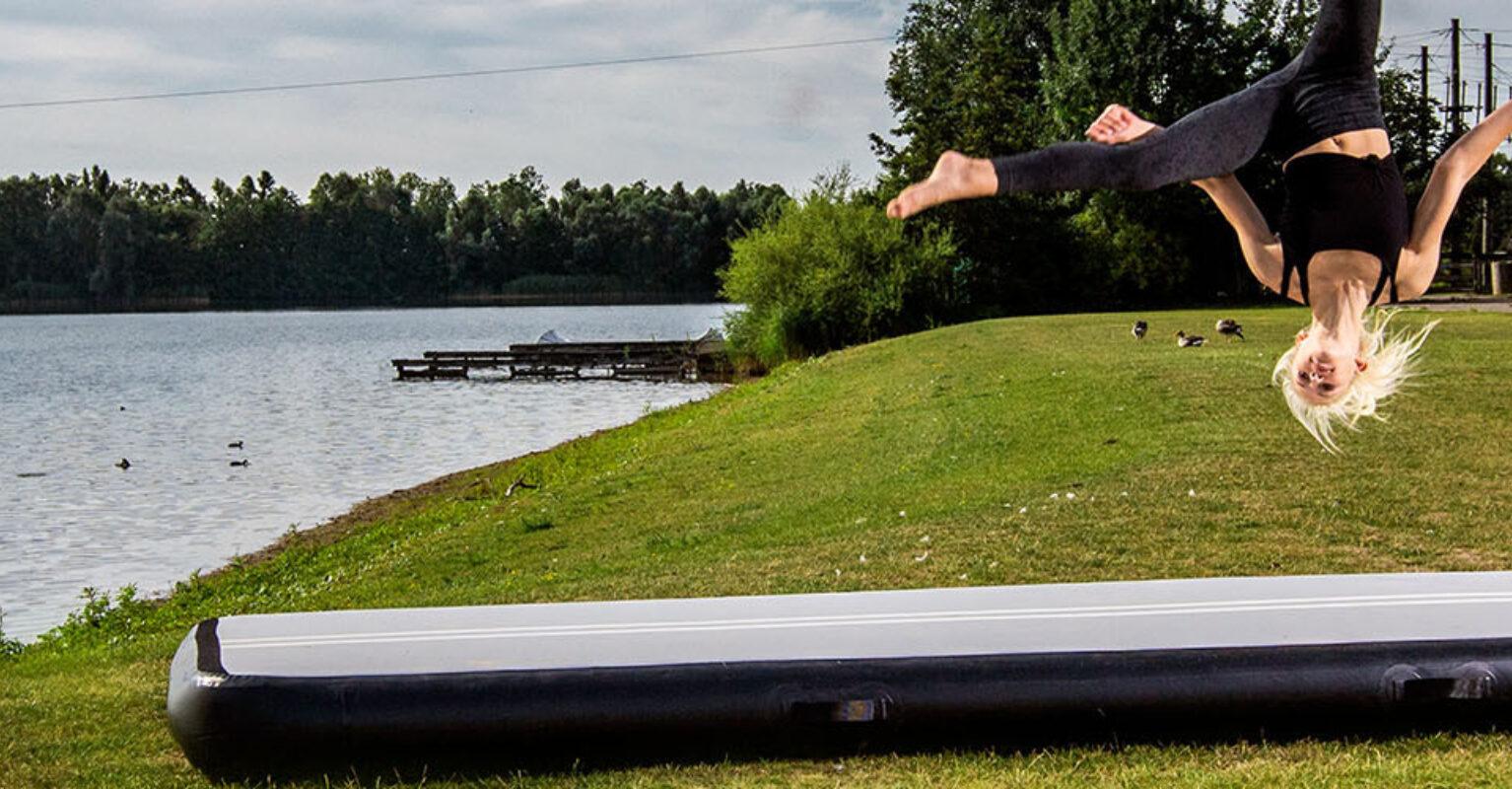 Gymnast performs a flip on a BERG AirTrack gymnastics mat outdoors – banner