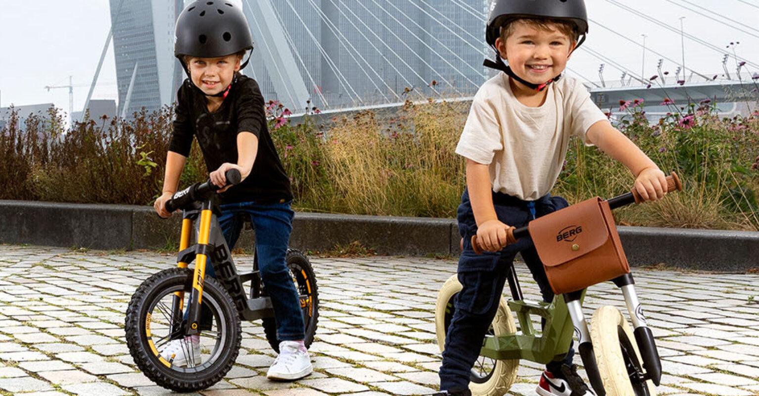 Two children ride BERG Biky balance bikes on a quay with a view of a bridge