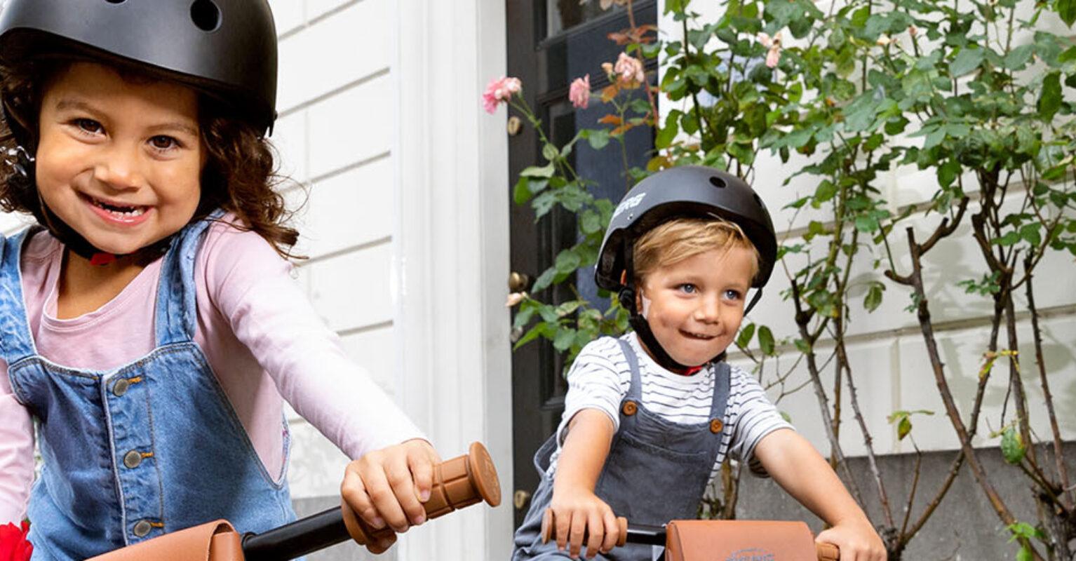 Two children riding a BERG Biky Retro balance bike in an urban setting