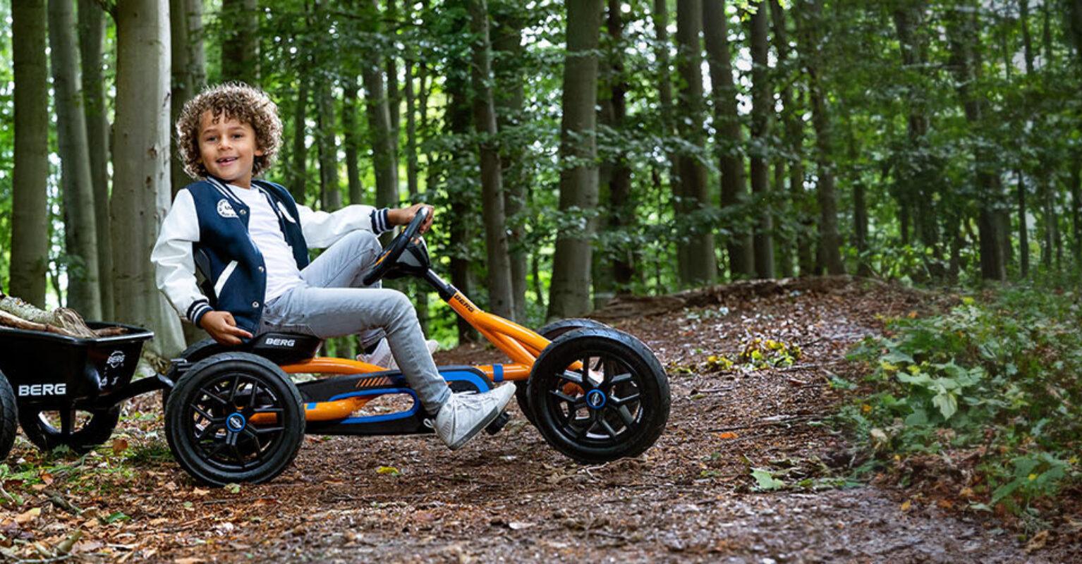 Child drives a BERG Buddy B-Orange go-kart with a trailer in a forest