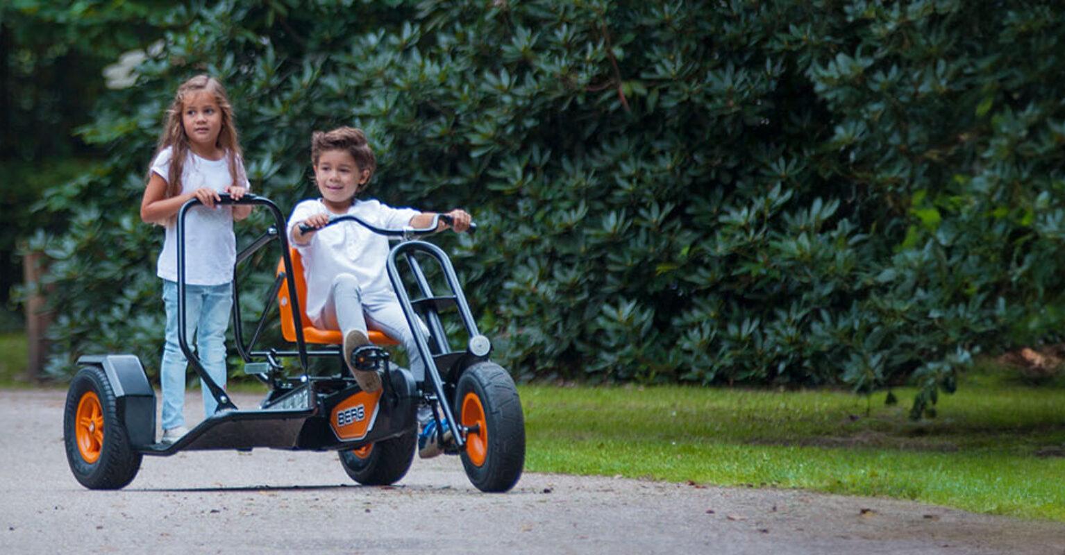 Twee kinderen rijden op een BERG Chopper driewiel skelter over een verharde weg