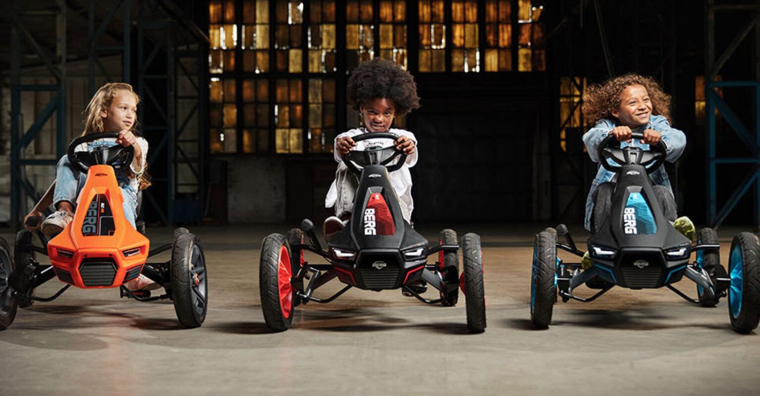 Three children ride different BERG Rally pedal karts in an industrial setting