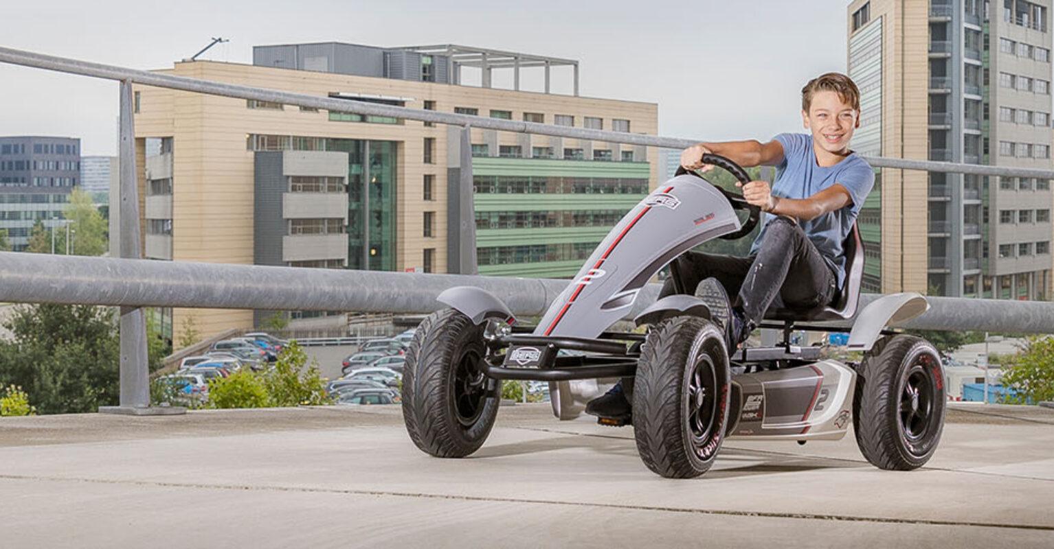 Child drives a BERG go-kart on a parking deck with an urban backdrop