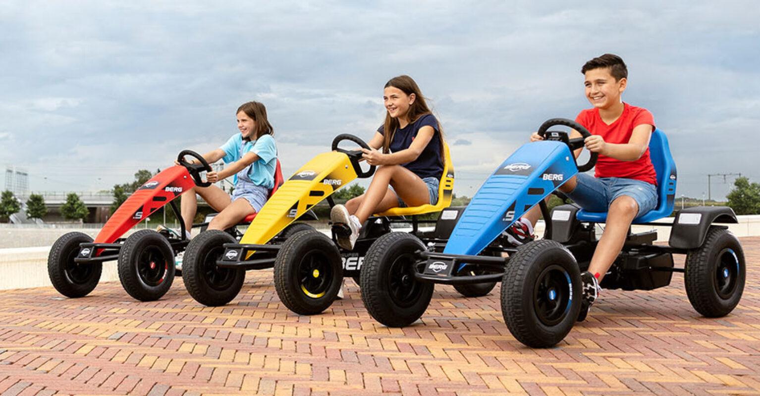 Three children riding BERG go-karts in different colors on a sunny day