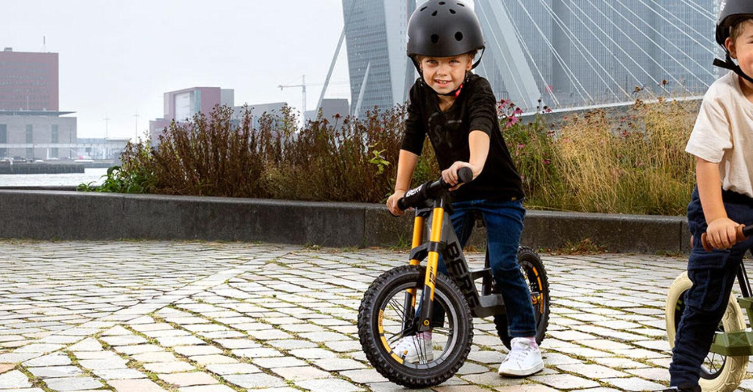 Banner with two children riding BERG Biky balance bikes in an urban setting